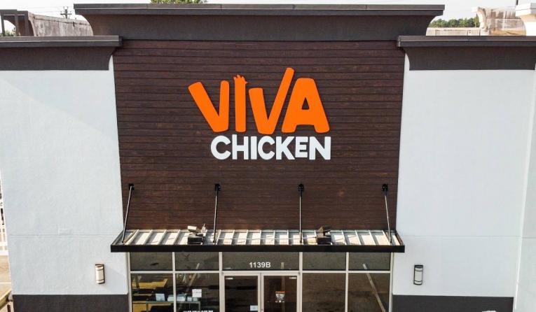 Storefront of Viva Chicken restaurant with a large orange and white sign above the entrance, featuring modern design elements and a glass door labeled 